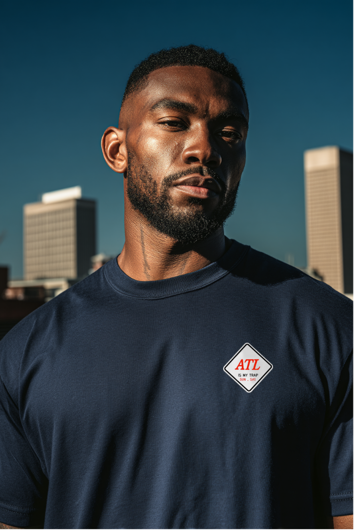 Man wearing a navy blue t-shirt with embroidered atl is my trap sun-sat logo against an urban skyline